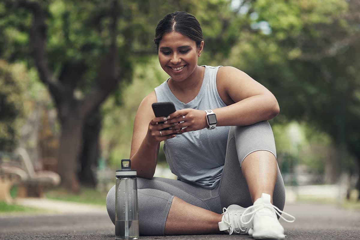 woman sitting outside in workout clothes looking at her phone and smiling after Laparoscopic surgery in Marion and Mount Vernon, IL