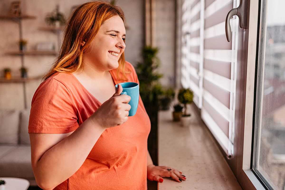 woman looking out a window holding a mug and smiling before medical weight loss in Marion and Mount Vernon